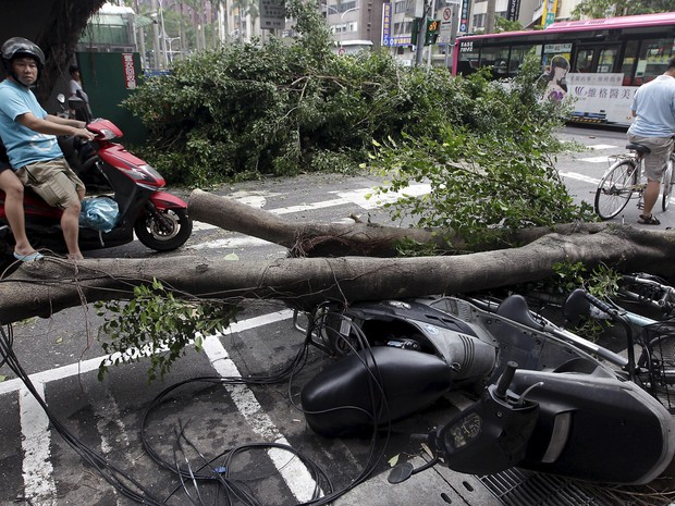 Pessoas passam por árvores desenraizadas e motocicletas danificadas após passagem do tufão Dujuan em Taipei, no Taiwan. Centenas de milhares de famílias ficaram sem água e mais de um milhão sem energia. Três pessoas morreram e mais de 300 ficaram feridas (Foto: Pichi Chuang/Reuters)