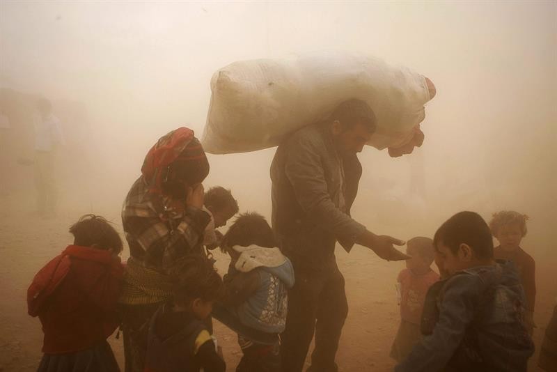 Refugiados sírios enfrentam uma tormenta de areia enquanto esperam para cruzar a fronteira com a Turquia