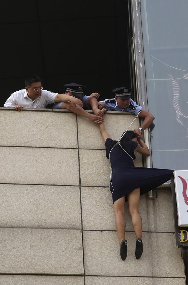 Policiais impedem que mulher pule de placa publicitária nesta quarta-feira (14) em Pequim (Foto: China Daily/Reuters)