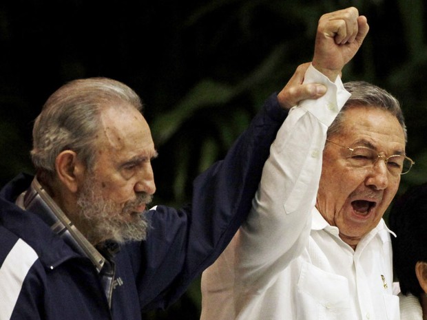 O ex-presidente de Cuba, Fidel Castro, ergue o braço do irmão e atual mandatário, Raul Castro, enquanto os dois cantam o hino do socialismo internacional durante o 6º Congresso do Partido Comunista, em Havana. (Foto: AP)