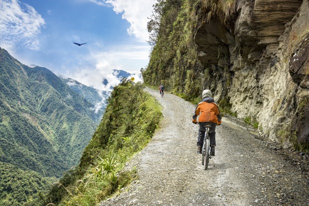 Bike adventure travel photo. Bike tourists  ride on the "road of death"  downhill track  in Bolivia. In the background sky circles a condor over the scene. (Foto: Getty Images/iStockphoto)