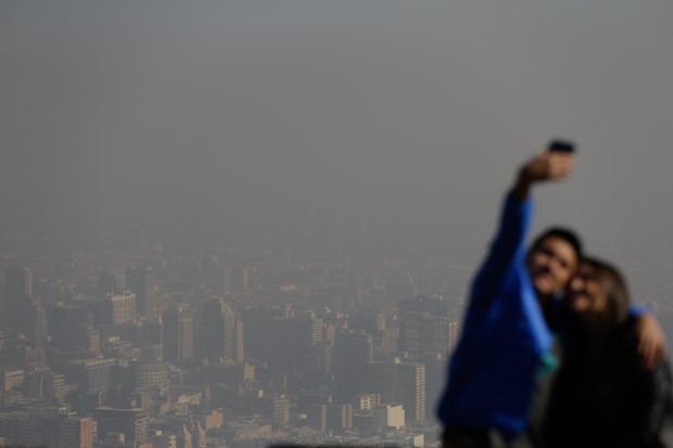 Turistas tiram uma &#39;selfie&#39; com o centro de Santiago, no Chile, ao fundo. Autoridades declararam estado de emergencia nesta segunda-feira (22) por causa do alto nível de poluição no ar (Foto: Jorge Saenz/AP)