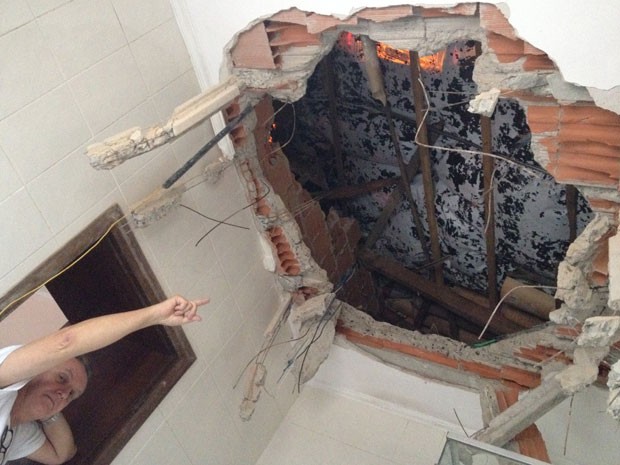 Quase um mês depois, Ricardo Fuchs aponta para buraco no teto do banheiro por onde passou rotor, que destruiu detalho e estrutura de concreto até parar no piso (Foto: Kleber Tomaz / G1)