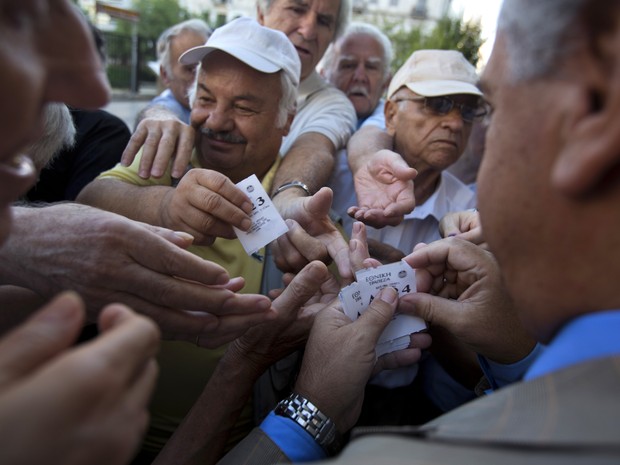Funcionário distribui senhas a aposentados no Banco Nacional da Grécia, em Atenas, para que eles possam sacar até € 120 de seus benefícios (Foto: Emilio Morenatti/AP)