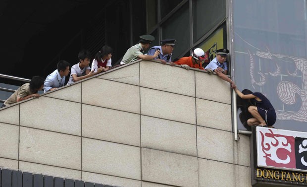 Policiais impedem que mulher pule de placa publicitária nesta quarta-feira (14) em Pequim (Foto: China Daily/Reuters) Policiais impedem que mulher pule de placa publicitária nesta quarta-feira (14) em Pequim (Foto: China Daily/Reuters)