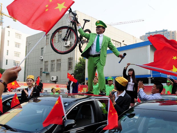 O bilionário chinês Chen Guangbiao segura bicicleta no topo dos carros comprados para donos de veículos danificados em protesto (Foto: AFP)