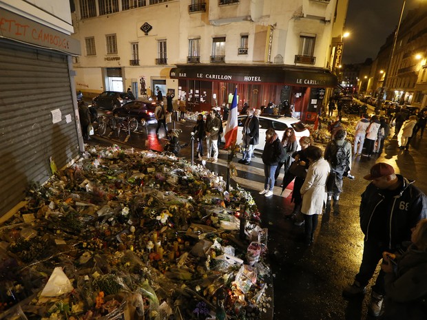 Pessoas se reúnem em memorial aos mortos em ataques terroristas em frente ao café Carillon (direita) e o restaurante Petit Cambodge (esquerda), no cruzamento das ruas Bichat e Alibert, em Paris, na sexta (20) (Foto: AFP Photo/Thomas Samson)
