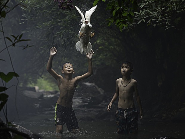 4) Sete prêmios por mérito também foram concedidos. Um deles foi para esta foto de Sarah Wouters, de dois meninos tentando pegar um pato em um riacho na província de Nong Khai, na Tailândia. (Foto: Sarah Wouters/National Geographic Traveler Photo Contest)