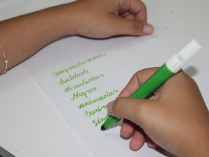 Jovem escreve no pedaço de papel qualidade das amigas (Foto: Gilcilene Araújo/G1)