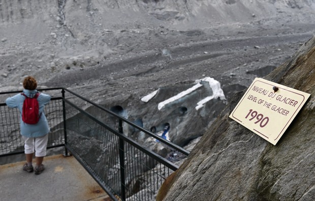 Visitante olha para caverna do Mar de Gelo; placa indica nÃ­vel da geleira em 1990 (Foto: AFP Photo/Philippe Desmazes)