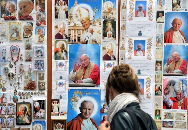 Mulher passa por posteres e cartões postais com a imagem do Papa João Paulo II em Roma (Foto: Stefano Rellandini/Reuters)