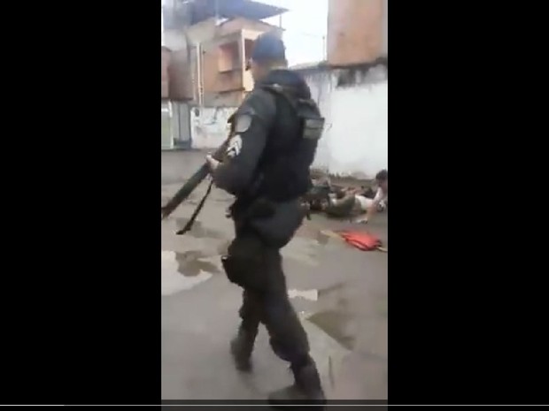Policial aparece caregando fuzil enquanto grupo é submetido à prática de exercícios físicos humilhantes (Foto: Reprodução Internet)