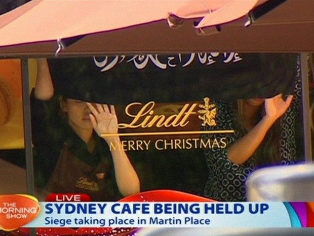 Pessoas seguram uma bandeira com escritas aparentemente árabes na vitrine da cafeteria onde um homem armado fez reféns em Sydney, na Austrália, em imagem reproduzida de uma emissora local (Foto: AP/Channel 7)