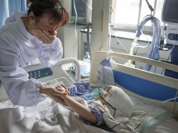 Mulher se emociona segurando a mão da menina Hanhah, de 3 anos, após ela se recuperar de uma cirurgia na qual 3 peças de titânio substituíram parte de seu crânio em Changsha, na China. A menina sofre de hidrocefalia e precisará passar por novas operações (Foto: Reuters/Stringer)
