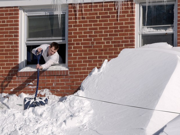   Shawn Covelly tira neve de frente de sua janela em Towson, no estado de Maryland, neste domingo  (Foto: AP Photo/Steve Ruark)