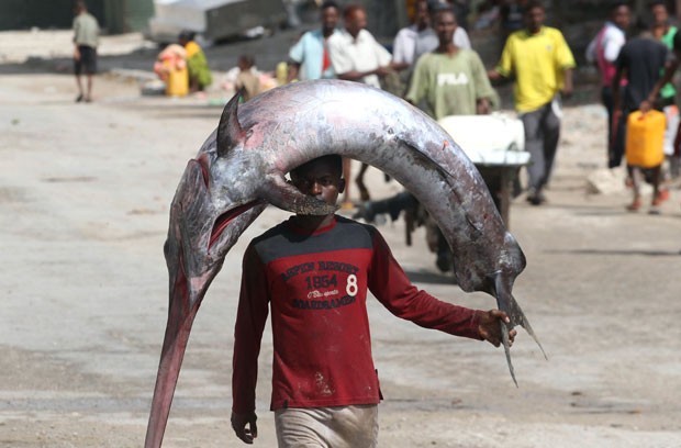 Um pescador foi flagrado nesta terça-feira (18) carregando um peixe-espada sobre a cabeça enquanto o levava para ser vendido em um mercado de Mogadíscio, na Somália. (Foto: Ismail Taxta/Reuters)