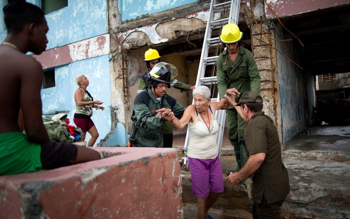 Bombeiros ajudam uma senhora a recuperar algumas roupas de sua casa que foi destruída pelo furacão Matthew em Baracoa, Cuba