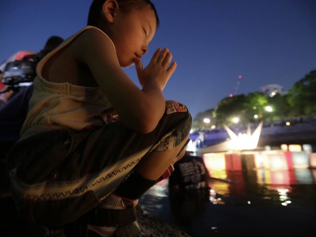 Menino faz oração após colocar uma lanterna japonesa de papel no rio Motoyasu, diante do Domo da Bomba Atômica em Hiroshima, durante memorial dos 70 anos da explosão da bomba que deixou 140 mil mortos na cidade ao fim da II Guerra Mundial (Foto: Eugene Hoshiko/AP)