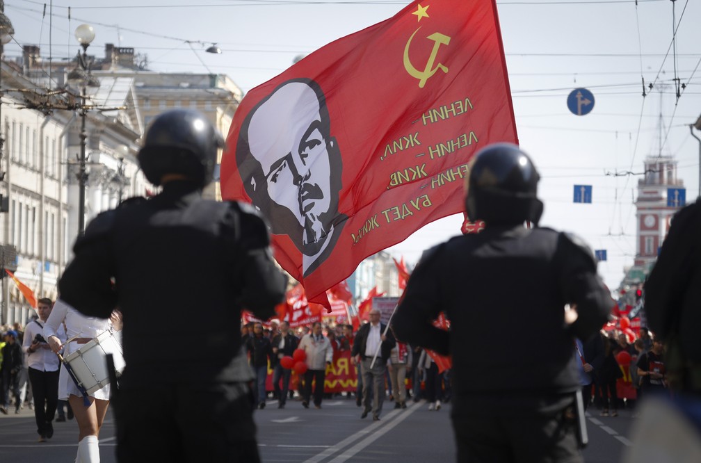 Apoiadores do partido comunista russo carregam uma bandeira com o rosto de Lênin durante os protestos de 1º de maio em São Petersburgo, na Rússia. — Foto: Dmitri Lovetsky/AP