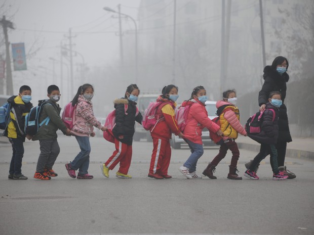 Crianças usando máscaras contra poluição atravessam a rua em Jinan, na província de Shandong, na China, nesta quinta-feira (24) (Foto: AFP)