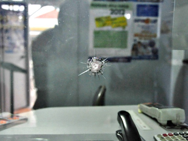 O vidro do caixa ficou trincado e estilhaços da bala no chão do local (Foto: Márcio Rogério/Nova News)