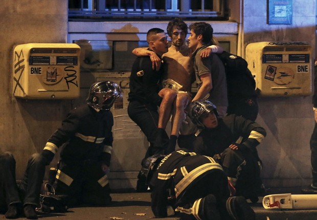 Membros da brigada de incêndio ajudam um homem ferido perto da sala de concertos Bataclan, após um ataque que deixou mortos e feridos em Paris (Foto: Christian Hartmann/Reuters)
