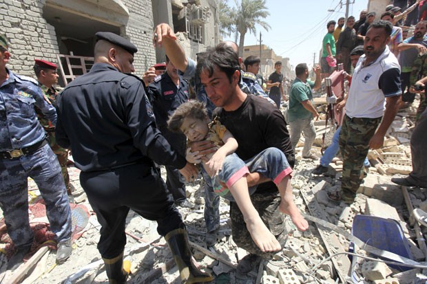 Homem carrega criança achada debaixo de destroços após casa ser bombardeada por engano em Bagdá nesta segunda-feira (6) (Foto: Reuters)