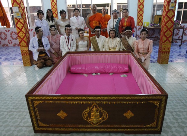 Casais posam próximos a caixão onde irão se deitar durante cerimônia de casamento na Tailândia (Foto: Chaiwat Subprasom/Reuters)