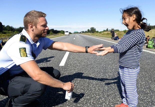 Policial dinamarquês brinca com menina migrante que caminhava pela rodovia E45, na fronteira germano-dinamarquesa, em direção à Suécia (Foto: Claus Fisker/ Scanpix Denmark/ AFP)