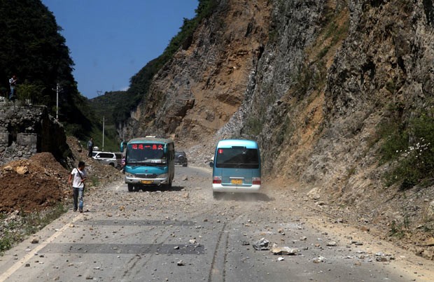 Ônibus passa por estrada em que pedras caíram após os terremotos desta sexta-feira (7) próximo à municipalidade de Zhaotong, entre as províncias chinesas de Yunnan e Guizhou (Foto: AFP)