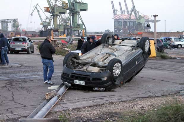 Homens observam carro capotado por fenômeno em Taranto nesta quarta-feira (28) (Foto: AP)