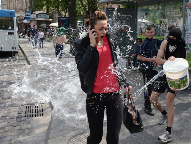 Mulher que falava ao celular é atingida por água jogada por jovem durante celebração na Ucrânia (Foto: Yuriy Dyachyshyn/AFP)
