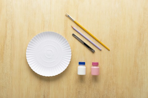 Você vai precisar de um prato de papelão (21 cm de diâmetro), um pincel, um lápis, um estilete, tinta branca e rosa