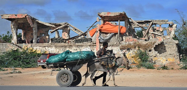 Homem caminha com animal e sacos de carvão perto de edifício atingido pela guerra na capital somali, em 23 de abril (Foto: Tony Karumba/AFP)