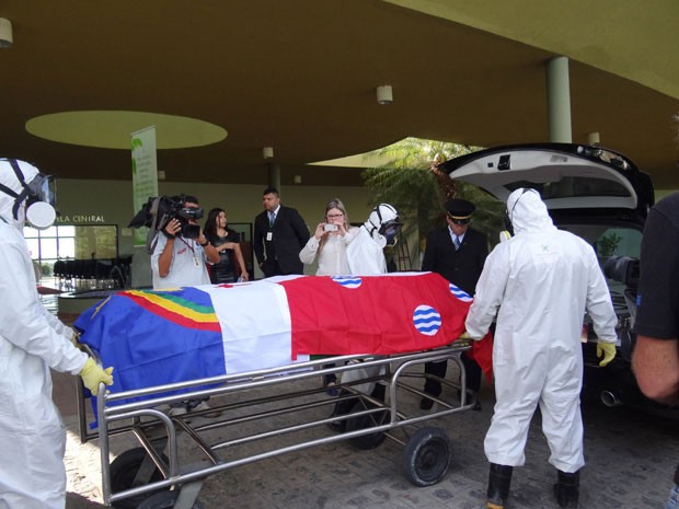 Usando roupas especiais, técnicos do cemitério para colocam corpo no carro (Foto: Katherine Coutinho/G1)