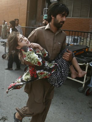 Homem socorre menina após ataque a posto de vacinação contra pólio no Paquistão (Foto: Khuram Parvez/Reuters)