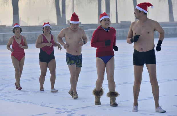 Com gorros de Papai Noel, participantes fazem aquecimento antes de nadar em lago congelado (Foto: Stringer/Reuters)