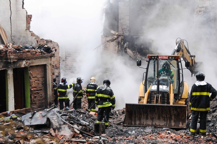 Bombeiros usam uma retroescavadeira para auxiliar nas buscas na Comunidade da Ilha, em São Paulo. No domingo (07), um grande incêndio ocorreu no local, matando pelo menos três pessoas 