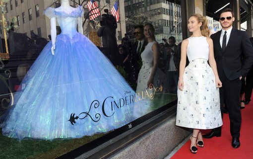 9 de março – Segundo look do dia! Outra vez ao lado de Richard Madden, Lily James posou em frente a uma vitrine temática de ‘Cinderela’ em Nova York, usando um vestido Dior branco e bem armadinho