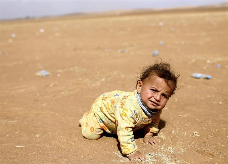  Um refugiado sírio bebê engatinha na areia próximo à fronteira da Turquia. Famílias sírias tentam fugir do país após ataques do Estado Islâmic