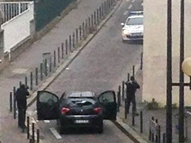 Homens armados são vistos saindo de um carro e apontando armas a um carro da polícia perto do escritório da revista satírica 'Charlie Hebdo', em Paris (Foto: Anne Gelbard/AFP)