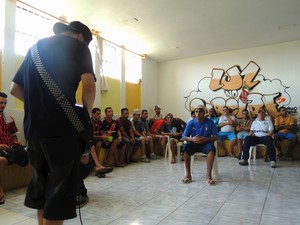 Uma pessoa toca guitarra enquanto os demais assistem.