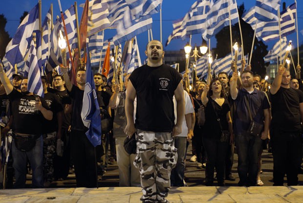 Militantes neonazistas gregos cantam o hino nacional do país em frente ao Parlamento, em Atenas, na noite desta quarta-feira (29) (Foto: AFP)