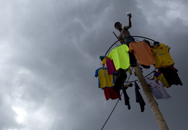 Homem comemora prêmio ao conseguir escalar pau de sebo em competição na Malásia. Participantes que chegam ao topo ganham prêmios como dinheiro e roupas (Foto: Mohd Rasfan/AFP)