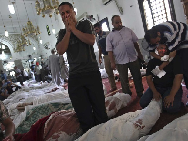 Homens choram à beira dos corpos de familiares mortos nos conflitos da véspera no Cairo. Ao lado de diversas outras vítimas, os corpos foram reunidos na mesquita El-Iman, no bairro de Nasr (Foto: Khalil Hamra/AP)