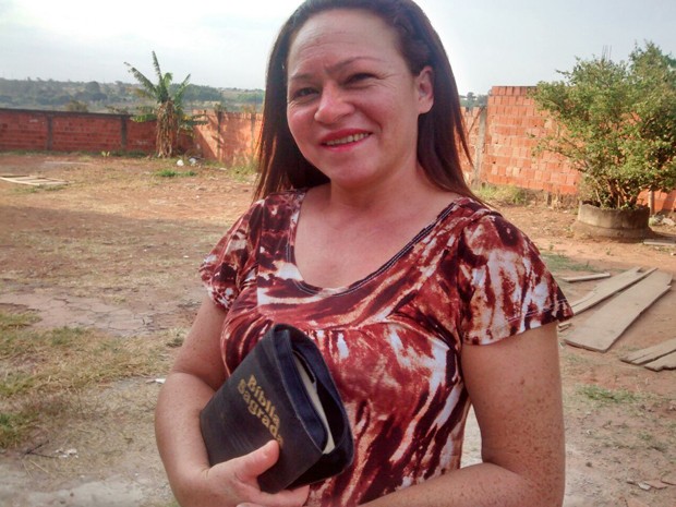 Ex-usuária de drogas que morou em bueiro no Distrito Federal, Odânia Batista Garcez segura bíblia no terreno da nova casa com o marido (Foto: Isabella Calzolari/G1)