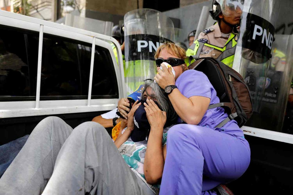 Mulheres tentam se proteger de gás lacrimogêneo lançado pela polícia durante manifestação em Caracas  (Foto: Carlos Garcia Rawlins/Reuters)