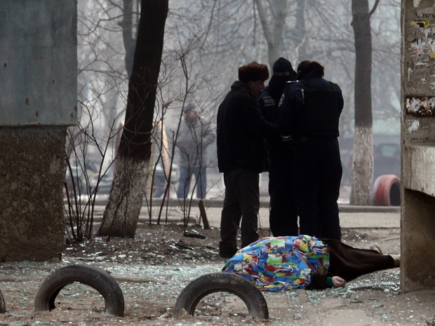  Policiais se reúnem ao lado de um corpo coberto depois de bombardeio na cidade portuária de Maiupol, na Ucrânia, neste sábado (24) (Foto: Stringer/AFP)