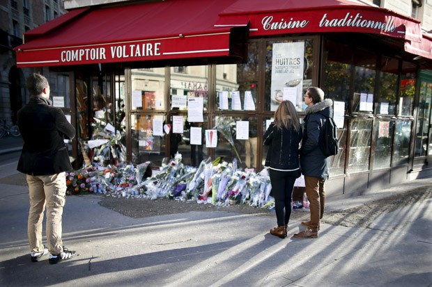 Pessoas param para olhar flores, velas e mensagens em homenagem às vítimas em frente ao café Comptoir Voltaire, um dos locais dos atentados terroristas em Paris, na França (Foto: Charles Platiau/Reuters)