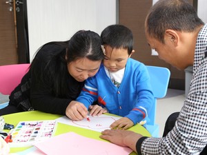 Mãe ajuda o filho a escrever; olhos artificiais se mexem mas menino não enxerga (Foto: C-Mer Dennis Lam Eye Hospital/AFP)